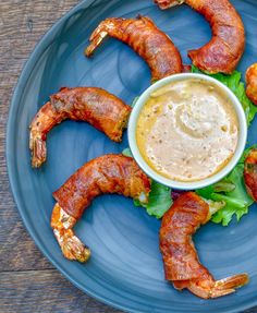 a blue plate topped with bacon wrapped in lettuce and dipping sauce on top