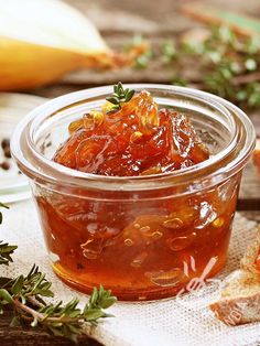 a glass jar filled with jelly sitting on top of a wooden table next to bread