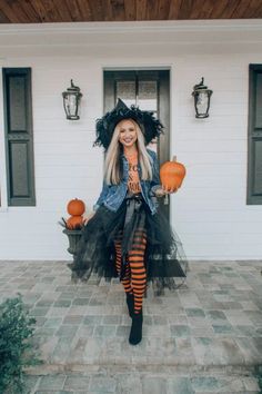 a woman dressed up as a witch standing in front of a house with pumpkins