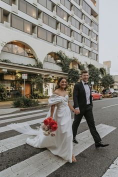 a bride and groom crossing the street in front of a hotel on their wedding day