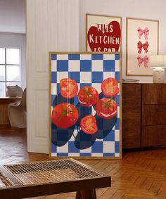 a kitchen area with a table, refrigerator and pictures on the wall above it that have tomatoes on them