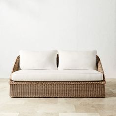 a wicker couch with two white pillows on the top and bottom, sitting in front of a wall