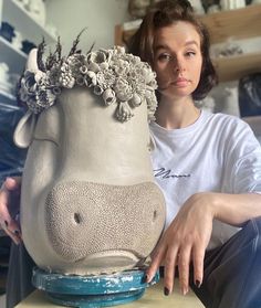 a woman sitting on a table with a vase in the shape of a hippo