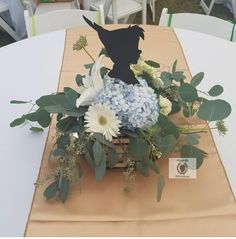 a table topped with a vase filled with flowers and greenery next to a sign