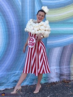 a woman in a red and white striped dress is holding some flowers while standing next to a wall