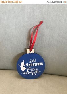 a blue ornament hanging from a red ribbon on a gray couch with the words, some vacations are worth waiting for us