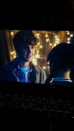 a young man standing in front of a computer screen with lights on the wall behind him