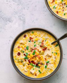 two bowls filled with corn and bacon soup on top of a table next to a spoon