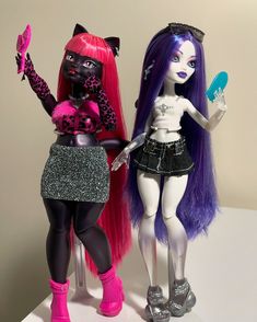 two dolls are standing next to each other on a white surface and one is holding a brush