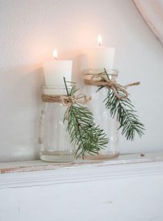 two candles are placed in glass jars with twine and pine needles tied to them