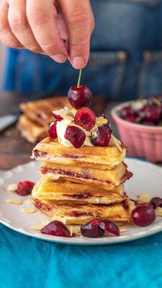 a stack of pancakes topped with cherries and whipped cream, being held by a person