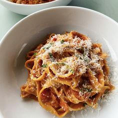 a plate of pasta with sauce and parmesan cheese on top, next to a bowl of bread