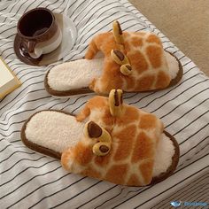 two giraffe slippers sitting on top of a bed next to a cup of coffee