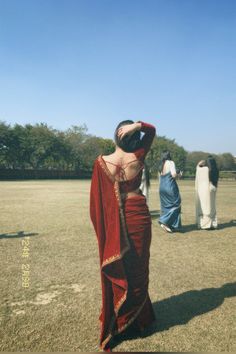 a woman in a red dress standing on top of a grass covered field next to other people