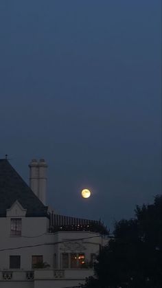 the full moon is setting over a white building