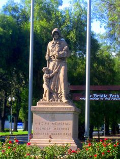 there is a statue in the middle of a park with flags and flowers around it