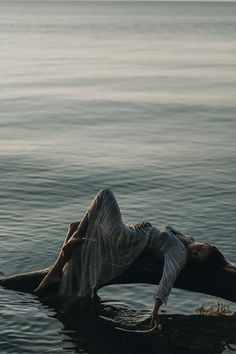 a woman laying on top of a log in the middle of the ocean with her head above water