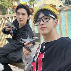 two young men sitting on a bench wearing animal ears and holding cell phones in their hands