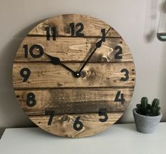 a clock made out of wooden planks with numbers on the face and hands, sitting next to a potted succulent