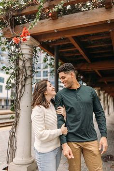 a man and woman standing next to each other in front of a tree with red flowers