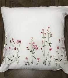 a white pillow with pink flowers embroidered on the front and back, sitting on a wooden floor