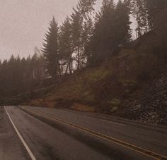 an empty road in the rain with trees on both sides and one car driving down it