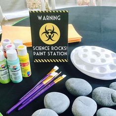 some rocks are sitting on a table with markers and paint bottles next to it is a sign that says science rocks paint station