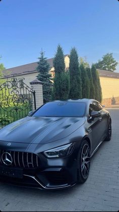 a black sports car parked in front of a gated driveway with trees and bushes