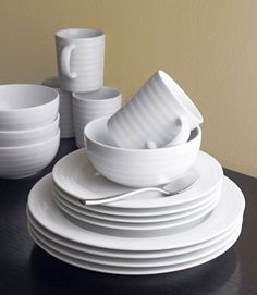 a stack of white dishes sitting on top of a wooden table next to cups and saucers