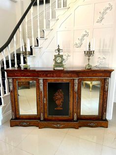 an ornate wooden cabinet with mirrors on the front and side doors, in front of a staircase