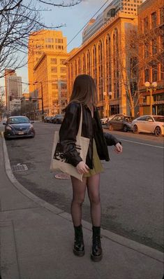 a woman is walking down the street with her hand in her pocket and wearing boots