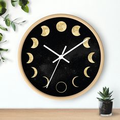 a clock with phases of the moon on it next to a potted green plant