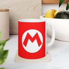 a red and white coffee mug sitting on top of a counter next to some fruit