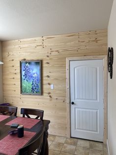 a dining room table and chairs with a painting on the wall behind it in front of a door