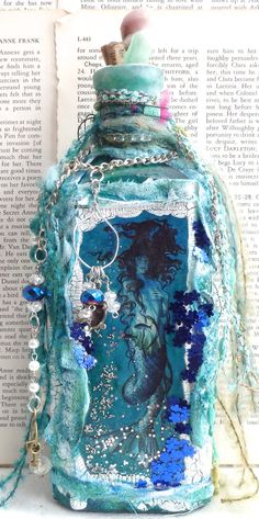 an altered glass bottle sitting on top of a book with chains hanging from it's sides