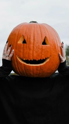 a person with their hands on the head of a pumpkin