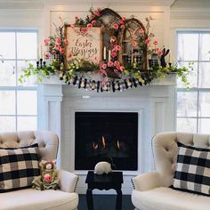 two chairs and a table in front of a fire place with flowers on the mantle