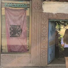 a woman standing in front of a building with a flag hanging from it's door