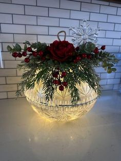 a glass bowl filled with red flowers and greenery on top of a white counter