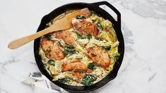 a skillet filled with pasta and chicken on top of a marble counter next to a wooden spoon