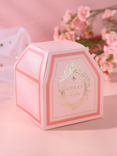 a small pink box with a gold crown on the top and flowers in the background