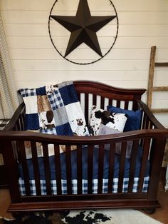 a wooden crib with blue and white bedding in front of a wall mounted star