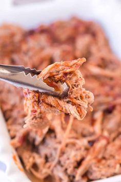 a spoon full of pulled pork on top of a casserole dish with sauce