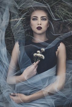 a woman is sitting in the grass with her hands on her chest and holding a flower