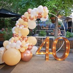 the number forty is made out of balloons and lit up in gold, white and silver