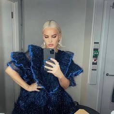 lady in blue dress looking at cell phone while standing in front of mirror with reflection