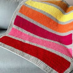 a crocheted blanket sitting on top of a couch next to a gray pillow