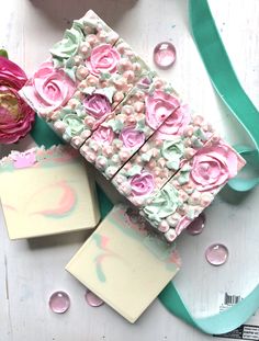 two soap bars with flowers on them next to a ribbon and some water droplets in the background