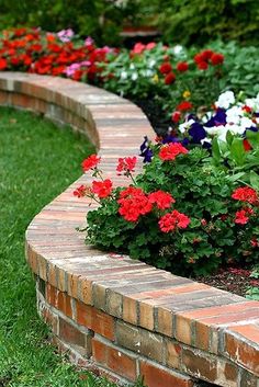 a flower garden with red and white flowers growing in it's center, surrounded by brick edgings