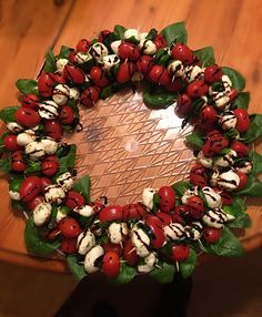 a wreath made out of tomatoes and spinach leaves on a wooden table with white chocolate drizzles